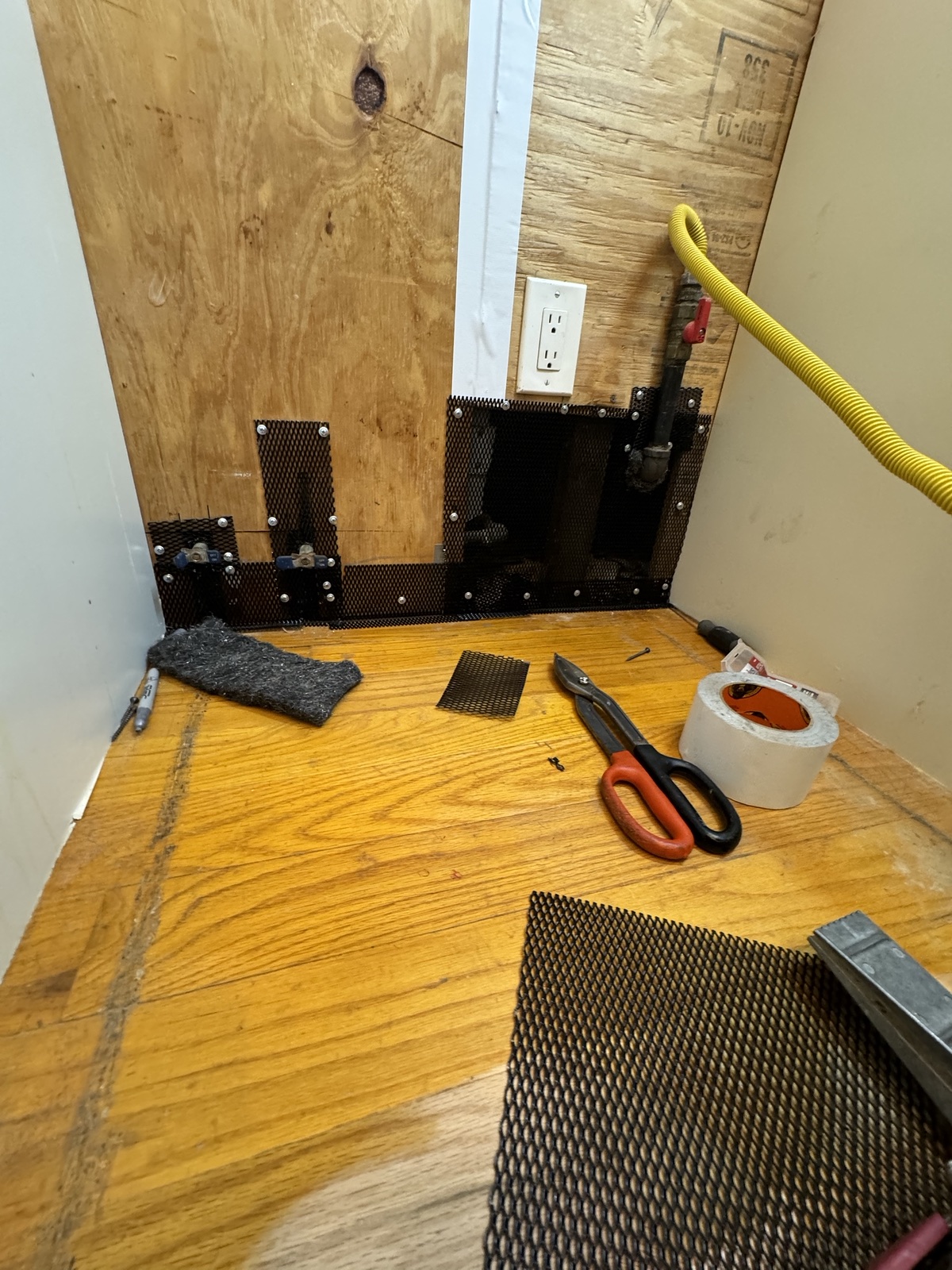 Black screening fastened around low wall openings and pipework behind a stove
